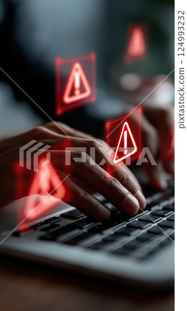 person typing on laptop with glowing red warning icons, symbolizing cybersecurity threats person typing on laptop with glowing red warning icons, symbolizing cybersecurity threats 124993232