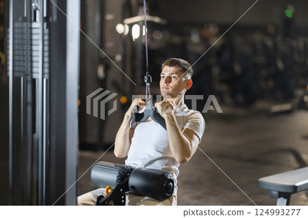 During training session in mini group of athletes, man exercises on cable crossover machine During training session in mini group of athletes, man exercises on cable crossover machine 124993277