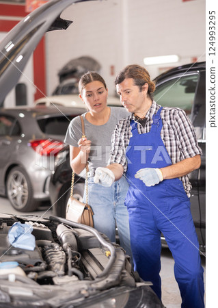 Woman talking to auto mechanic in uniform about repairing his car engine in auto repair shop 124993295