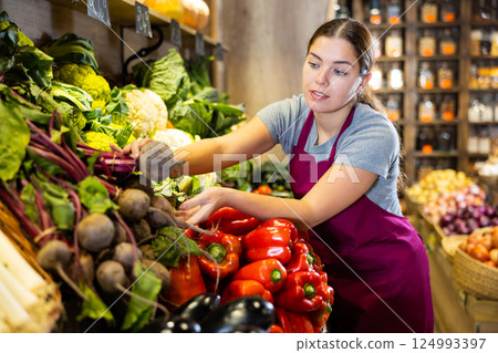 Female grocery store worker lays out bell peppers on the counter and display case Female grocery store worker lays out bell peppers on the counter and display case 124993397