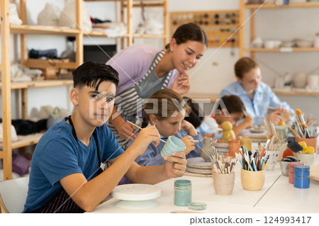 Teenage boy painting ceramic cupin pottery workshop 124993417