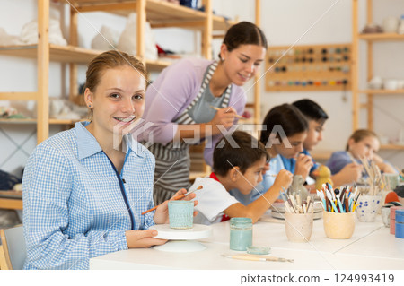 Teenage girl painting handmade ceramic cup with brush 124993419