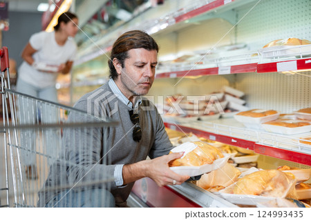 Man comparing packaged chicken in animal products section of store 124993435