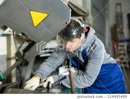 Young guy puts steel part on machine 124993489