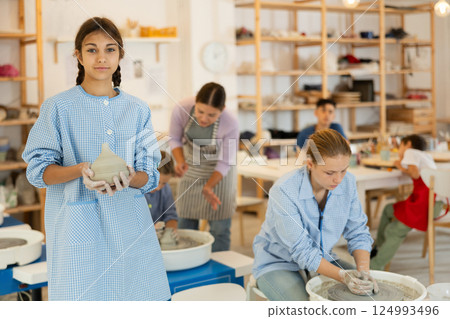 Girl holds a clay product against the background of students and a teacher 124993496