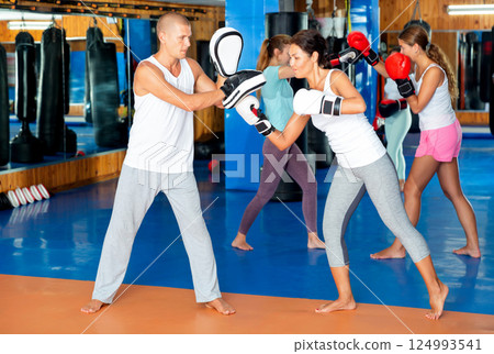 Asian woman in boxing gloves launching blows on punch mitts 124993541