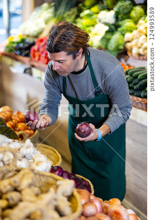 Male vegetable salesman in apron showing fresh red onions in market Male vegetable salesman in apron showing fresh red onions in market 124993589