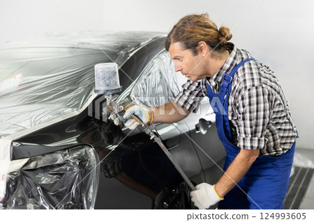 Adult male mechanic paints car with machine Adult male mechanic paints car with machine 124993605