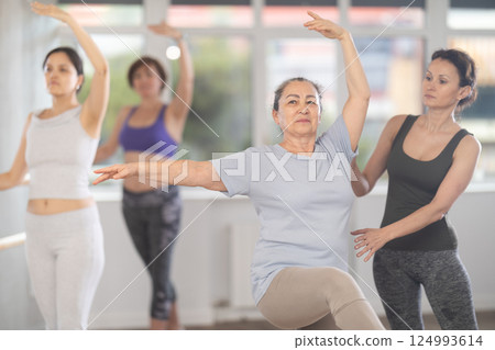 Dance instructor adjusting ballet pose of elderly female student 124993614