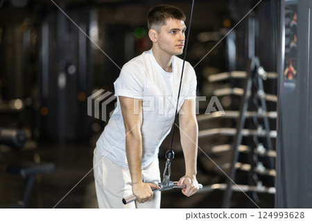 Guy performing triceps pushdowns on cable machine at gym 124993628