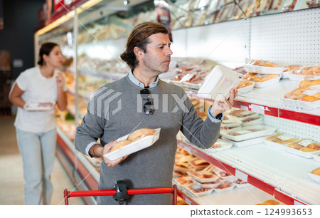Attentive customer chooses chicken meat in the meat department of supermarket Attentive customer chooses chicken meat in the meat department of supermarket 124993653