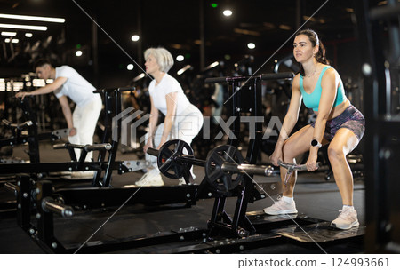 Woman performing deadlift on lever-loaded machine in gym 124993661