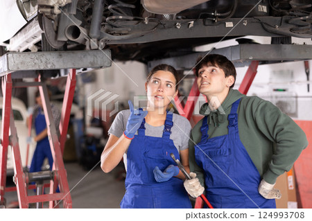 Two young mechanics discussing car repairs under lifted vehicle 124993708
