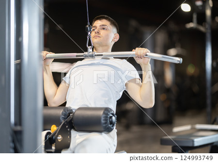 Guy doing wide-grip lat pulldown on cable machine in gym 124993749