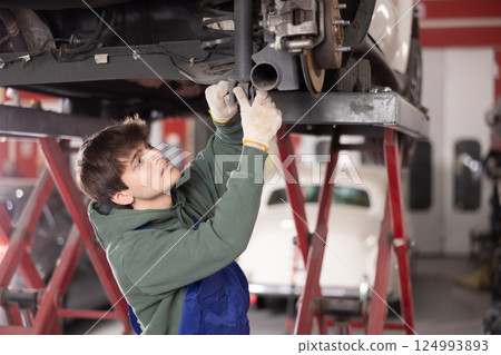 Young guy mechanic repairs underbody of car 124993893