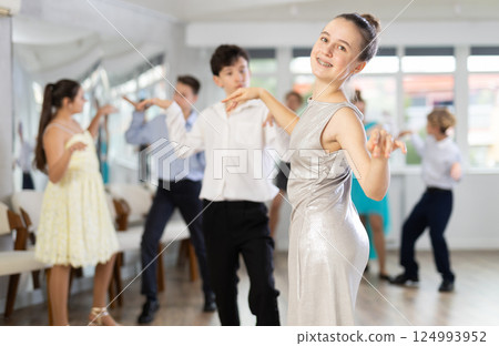Teen girl in elegant evening dress dances incendiary twist with boy partner during choreography lesson 124993952