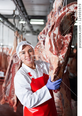 Female butchery worker checking hanging raw cow carcasses 124993979