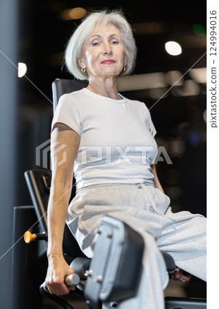 Older woman training on hip abduction machine at gym 124994016