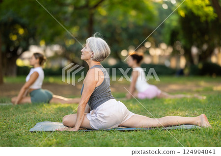 Senior woman practicing Ardha Kapotasana at group yoga training outdoors 124994041