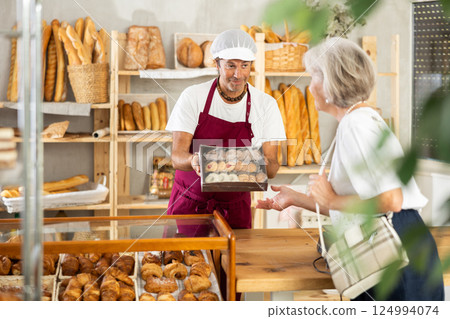 Male owner of bread shop shows for senior woman customer cookies in box 124994074