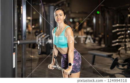Woman performing triceps pushdowns on cable machine in gym 124994318
