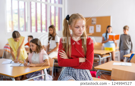 Upset tween girl sitting on table in schoolroom during recess 124994527