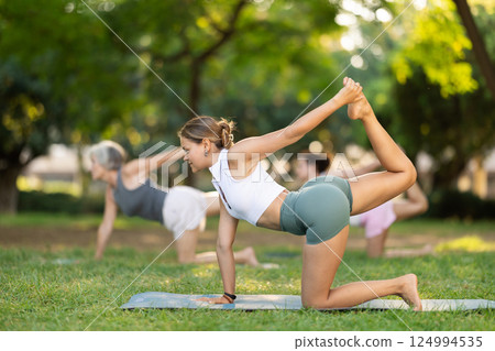 Girl performing Kneeling Bow pose in outdoor group yoga session 124994535
