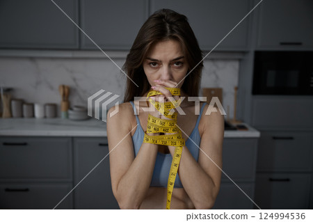 Sad female with tied hands with centimeter measuring tape on kitchen 124994536