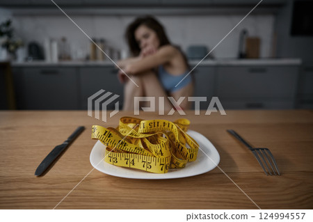 Depressed anorexic woman looking at plate with measuring tape served for dinner 124994557
