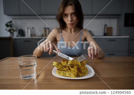 Skinny anorexic woman eating measuring tape showing lack of appetite 124994560
