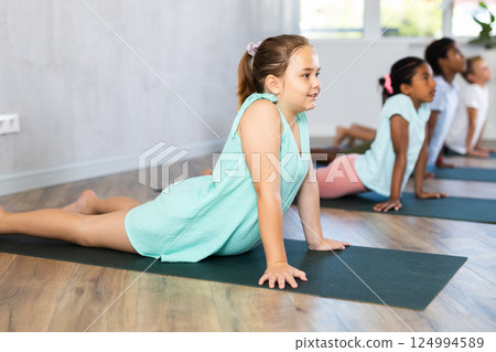 Children practicing yoga positions during group training in fitness center, performing stretching asana Urdhva Shvanasana 124994589