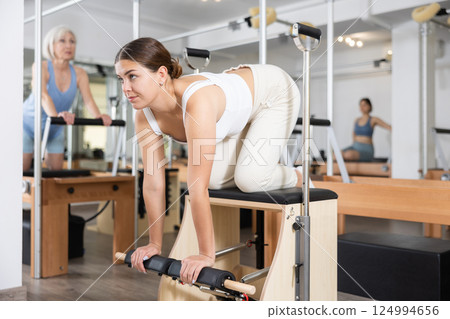 Young girl doing exercises on wunda chair in pilates studio Young girl doing exercises on wunda chair in pilates studio 124994656