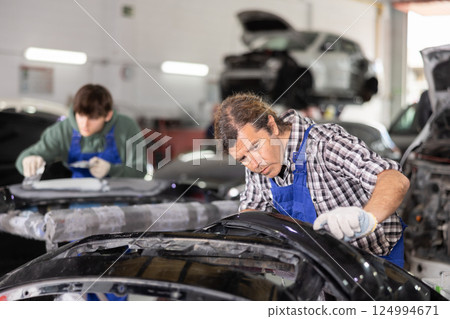 Experienced mechanic inspecting detached car bumper in workshop Experienced mechanic inspecting detached car bumper in workshop 124994671