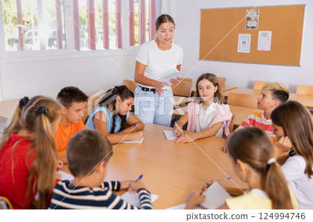 Teacher, together with group of schoolchildren, are looking for solution to complex tasck at round table in school classroom 124994746