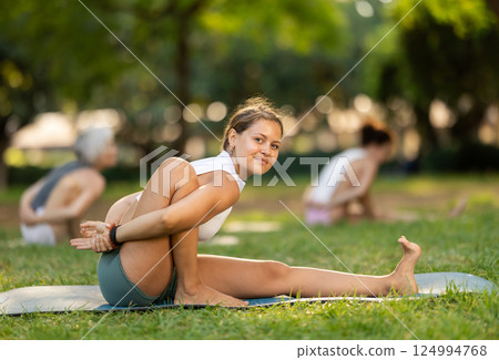 Young woman in sportwear with group of sporty adult people training stretching workout legs at city park together Young woman in sportwear with group of sporty adult people training stretching workout legs at city park together 124994768