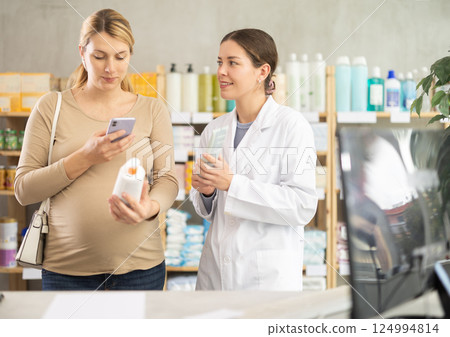 Pregnant woman using phone to check ingredients of cream with pharmacist guidance 124994814