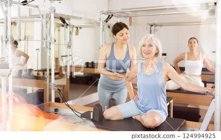 Female trainer checking and helping senior woman exercising on pilates reformer machine in health center Female trainer checking and helping senior woman exercising on pilates reformer machine in health center 124994925