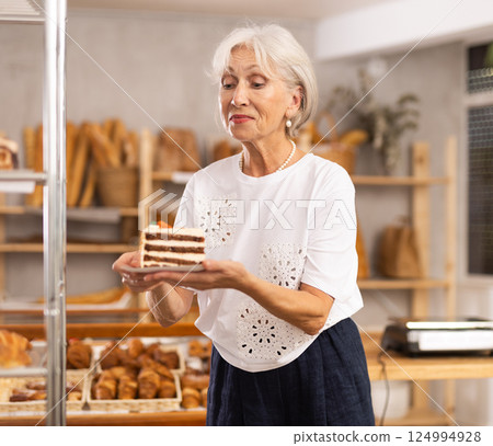 Pleased mature woman holding pastry on paper plate in bakery Pleased mature woman holding pastry on paper plate in bakery 124994928