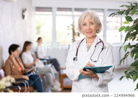 Elderly female doctor filling out papers in lobby of clinic Elderly female doctor filling out papers in lobby of clinic 124994966