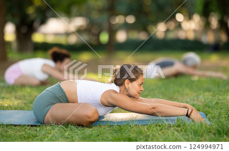 Young woman in sportwear with group of sporty adult people training stretching workout legs at city park together Young woman in sportwear with group of sporty adult people training stretching workout legs at city park together 124994971