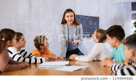 Positive female teacher explaining topic to tweens children during lesson in class of middle school Positive female teacher explaining topic to tweens children during lesson in class of middle school 124994980
