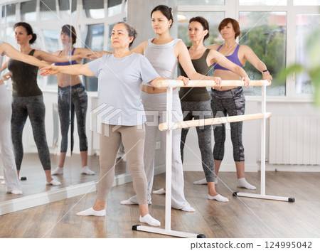 Women of different ages exercise near the ballet barre at group training session in batman batyu position 124995042