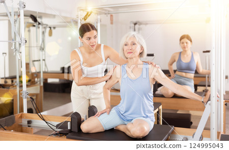 Aged woman practicing pilates on reformer with young female trainer 124995043
