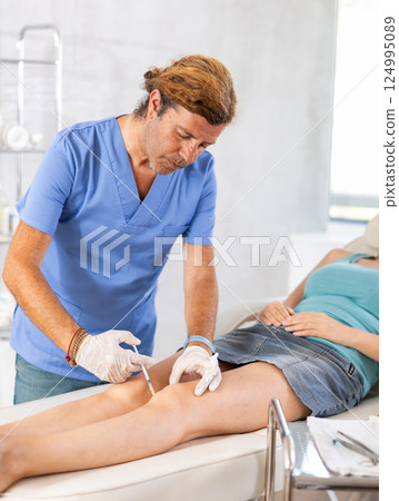 Male doctor making injection in leg of woman patient 124995089