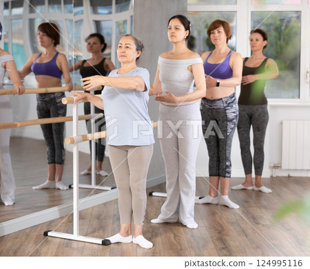 Senior woman practicing first position at barre in ballet studio Senior woman practicing first position at barre in ballet studio 124995116