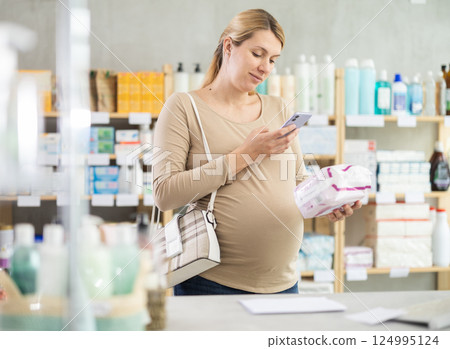 Pregnant woman in pharmacy scans QR code on feminine pad product Pregnant woman in pharmacy scans QR code on feminine pad product 124995124