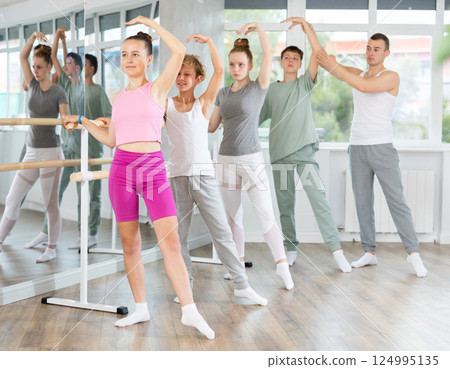 Teacher conducts class with teen girls and boys in ballet studio, observes doing Batman exercise. 124995135