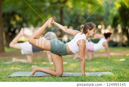 Happy sporty skilled young women going table pose of yoga with group in park at daytime 124995145