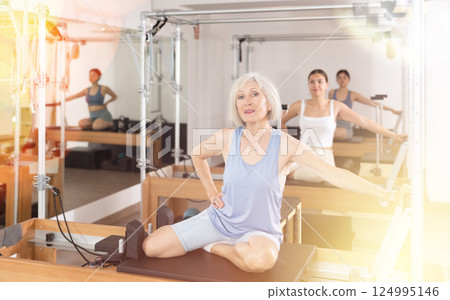 Mature woman practicing pilates stretching exercises on reformer at gym 124995146