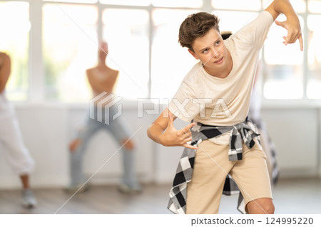 Teen guy together with group of teenage friends, learn to dance hip hop in choreographic hall. 124995220